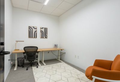 Small private office with a geometric rug, orange armchair, and dual-surface desk.
