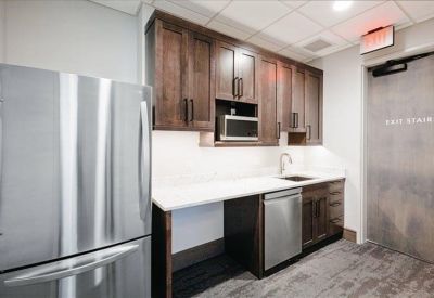 Compact kitchenette area with dark wood cabinets, stainless steel dishwasher, and white countertops.