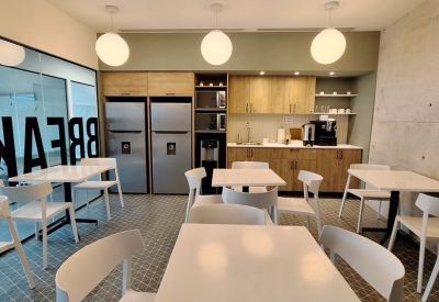 Office kitchen and dining area with wooden cabinetry, white tables, and spherical pendant lights.