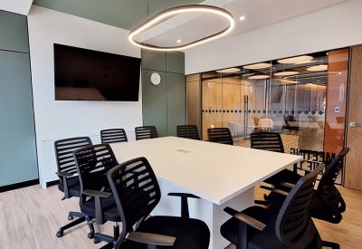 Spacious boardroom with a long white table, black chairs, and a large wall-mounted monitor.