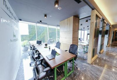 Bright coworking area with a long wooden desk, laptops, and floor-to-ceiling windows.