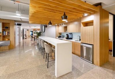 Sleek kitchen breakout area with a long white breakfast bar and wooden overhead features.