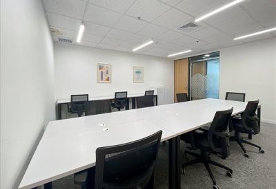 Bright office space with a large white table and black ergonomic mesh chairs.