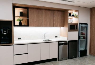 Modern office kitchen with white cabinetry, wood accents, and integrated appliances.