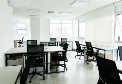 Bright open-plan office with white desks and black ergonomic chairs near large windows.