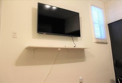 Meeting room corner with a large wall-mounted monitor and a white floating shelf.
