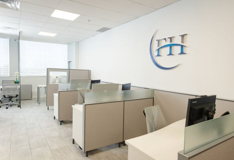 Open-plan workspace with cubicles, ergonomic chairs, and a branded logo on a white feature wall.