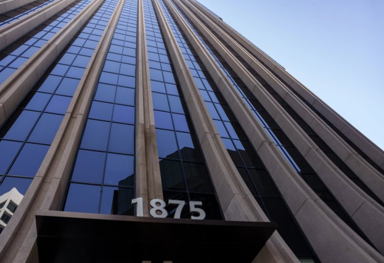 Looking up at the glass and stone facade of 1875 Century Park E against a clear blue sky.