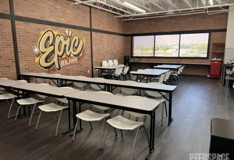 Spacious training room with multiple rows of tables, white chairs, and an Epic mural on a brick wall.