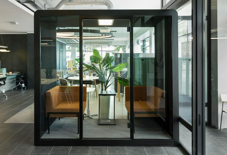 Modern interior at 100, King Street West featuring a glass meeting pod with tan seating and a large indoor plant.