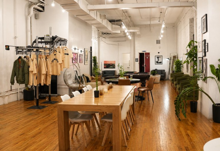 Large shared workspace featuring a long wooden table, white chairs, and clothing display.