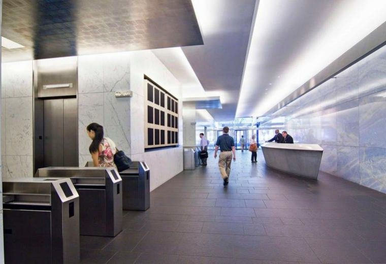 Sleek office reception lobby with high ceilings, security turnstiles, and a long service desk.