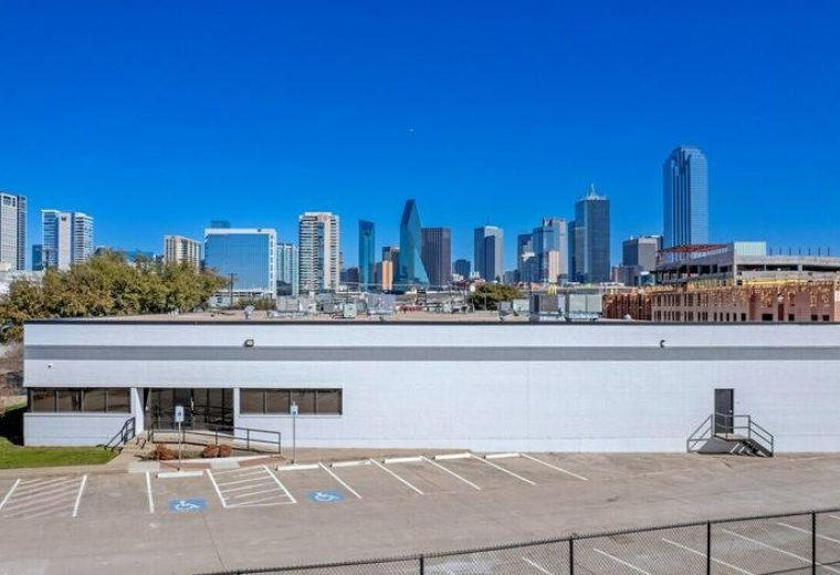 Exterior view of the white commercial building at 152 Continental Avenue with the Dallas skyline in the background.