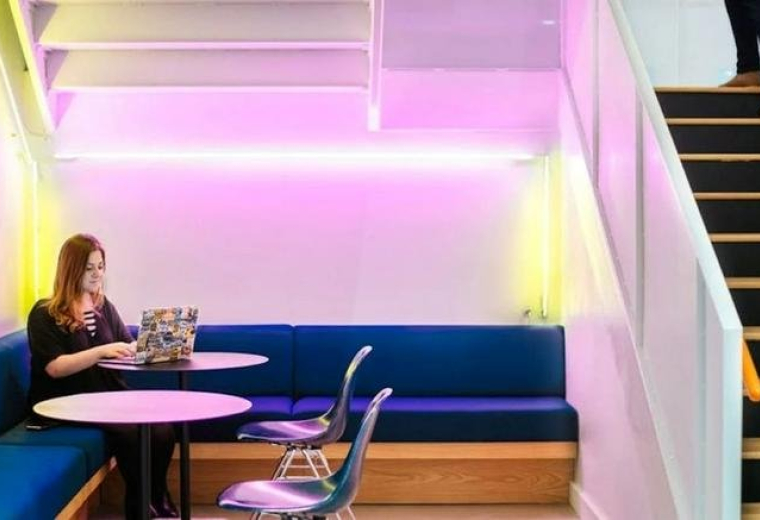 Breakout booth with blue seating and a woman working under pink neon lights at 154 W 14th Street, New York City.