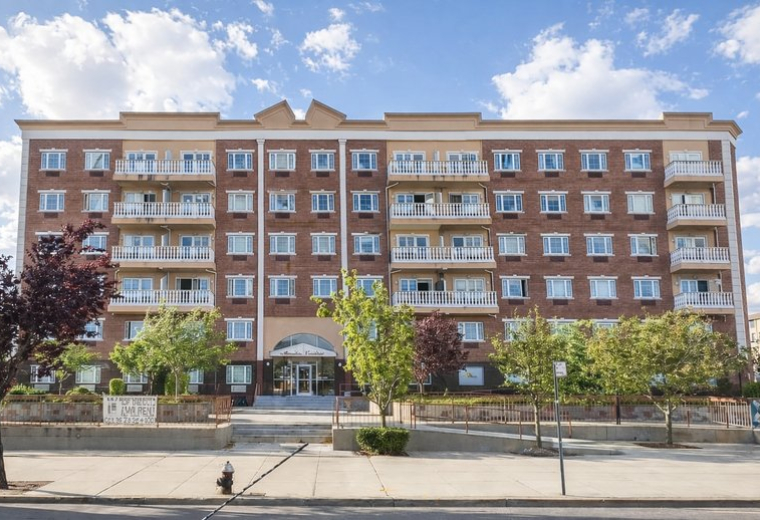 Close-up of the brick and tan facade of the Office on the Bay building with green trees in front.