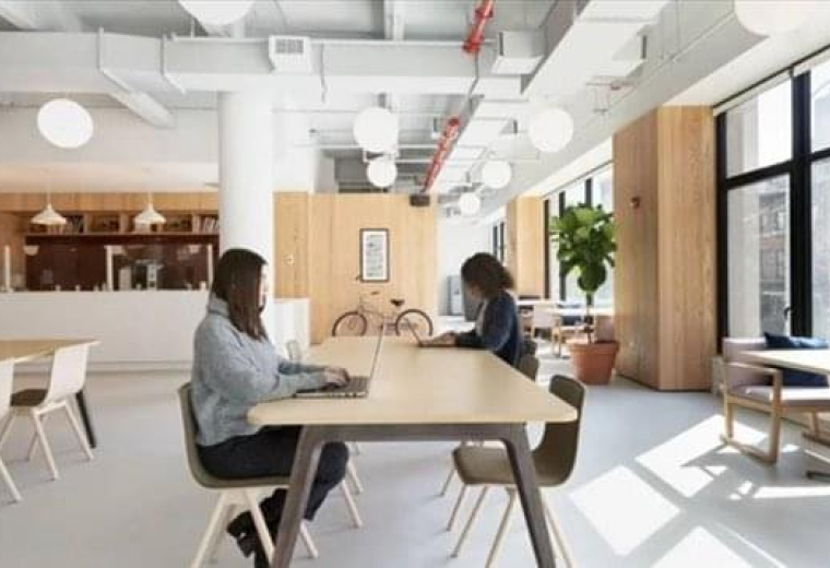 Spacious communal lounge at 413 West 14th Street, New York City with wooden tables and large windows.