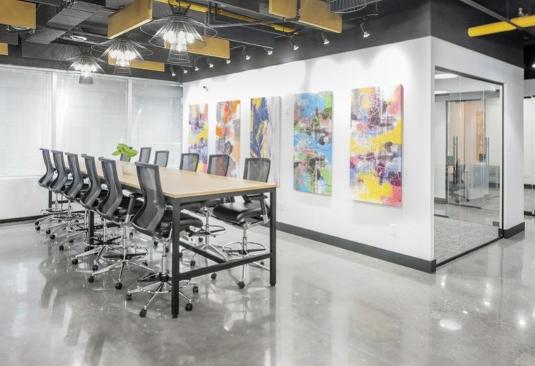 Large, high-topped meeting table with several stools and colorful abstract art on the wall.