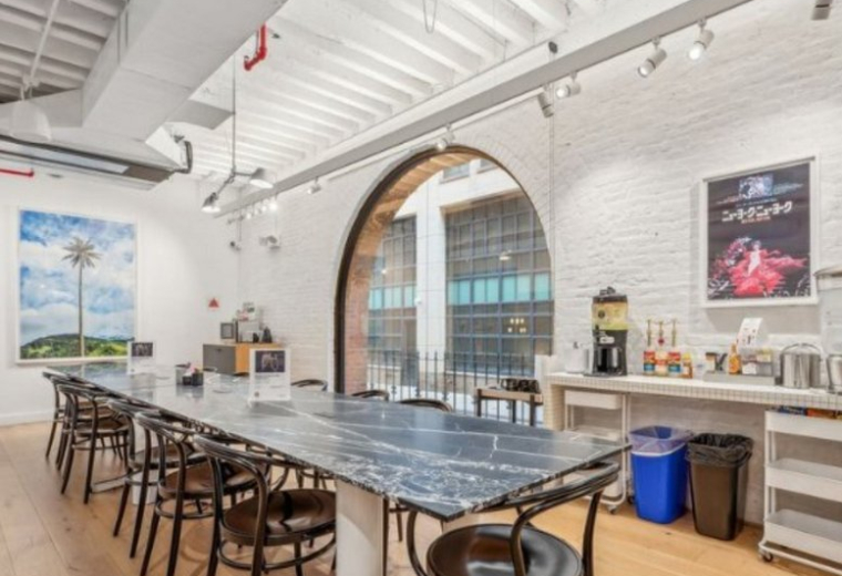 Communal dining area featuring a long marble table and a large architectural arched window.