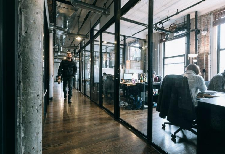 Industrial-style hallway at 71 5th Avenue, Manhattan, New York City featuring glass-walled offices and wood floors.
