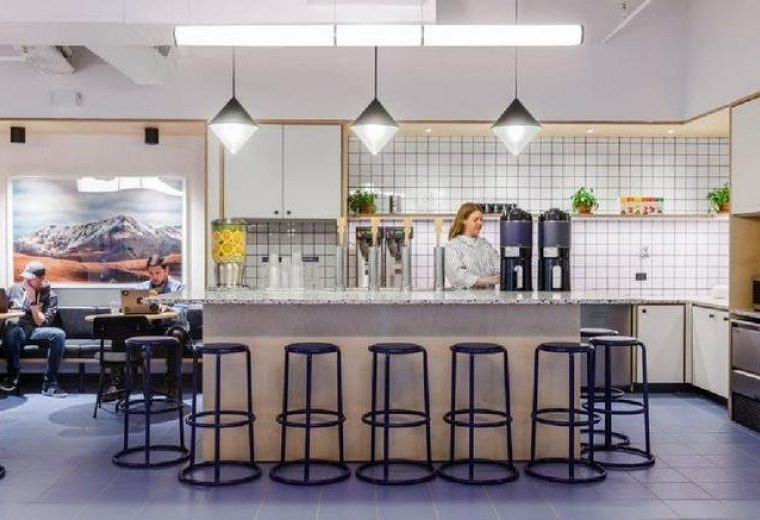 Spacious communal kitchen and cafe area at 750 Lexington Avenue with pendant lighting and blue stools.