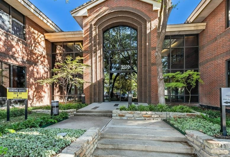 Exterior entrance of the brick building at 9535 Forest Ln featuring a large arched glass facade.