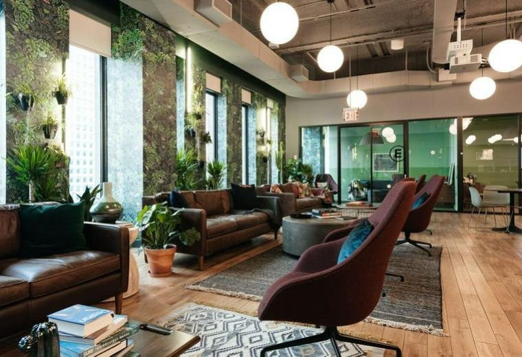 Spacious communal lounge at 85 Broad Street with leather sofas, hanging globe lights, and lush plant walls.