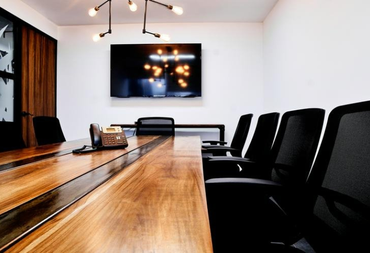 Sleek conference room at Kenex Plaza with a long wooden table and wall-mounted screen.