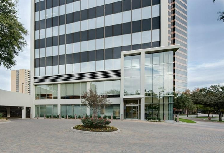 Modern building entrance with a glass-enclosed lobby and paved driveway.