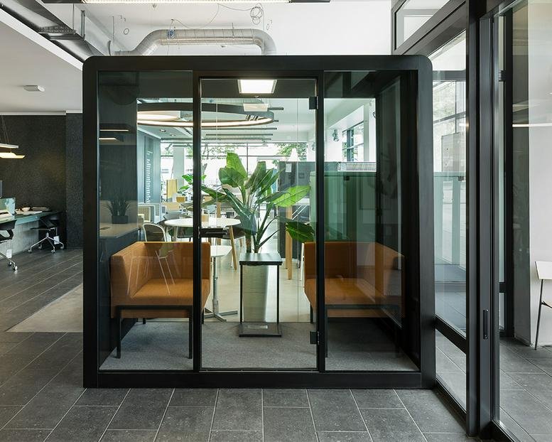 Modern interior at 100, King Street West featuring a glass meeting pod with tan seating and a large indoor plant.