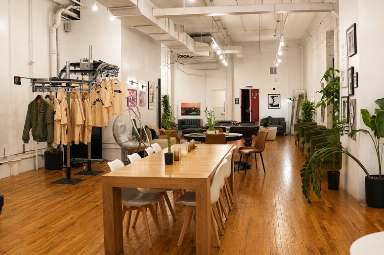 Large shared workspace featuring a long wooden table, white chairs, and clothing display.
