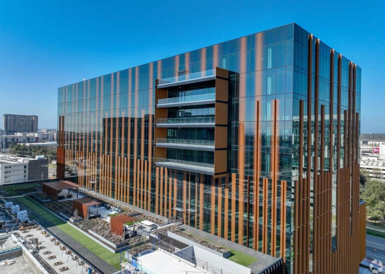 The glass-facade exterior of 11515 Burnet Road, 700 with bronze vertical accents and roof terrace.