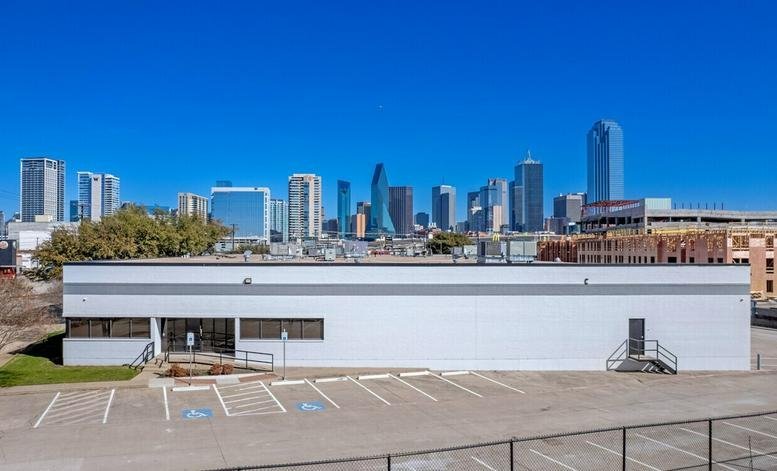 Exterior view of the white commercial building at 152 Continental Avenue with the Dallas skyline in the background.