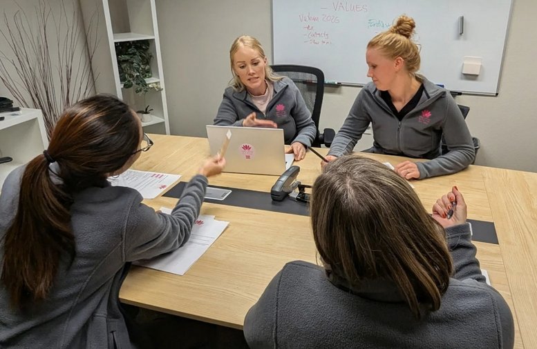 A team of four people collaborating around a light wood conference table in a bright meeting room.