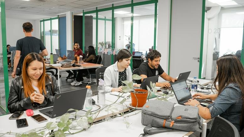 Bright shared office space with green-framed glass partitions and multiple workstations.