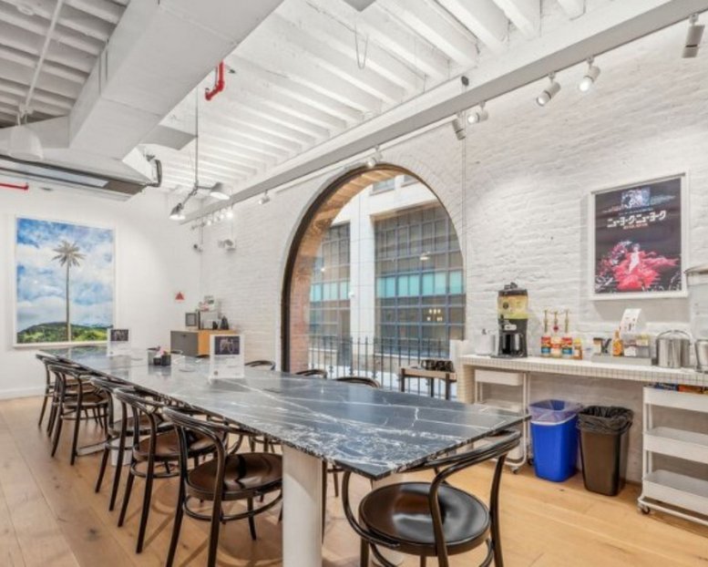 Communal dining area featuring a long marble table and a large architectural arched window.