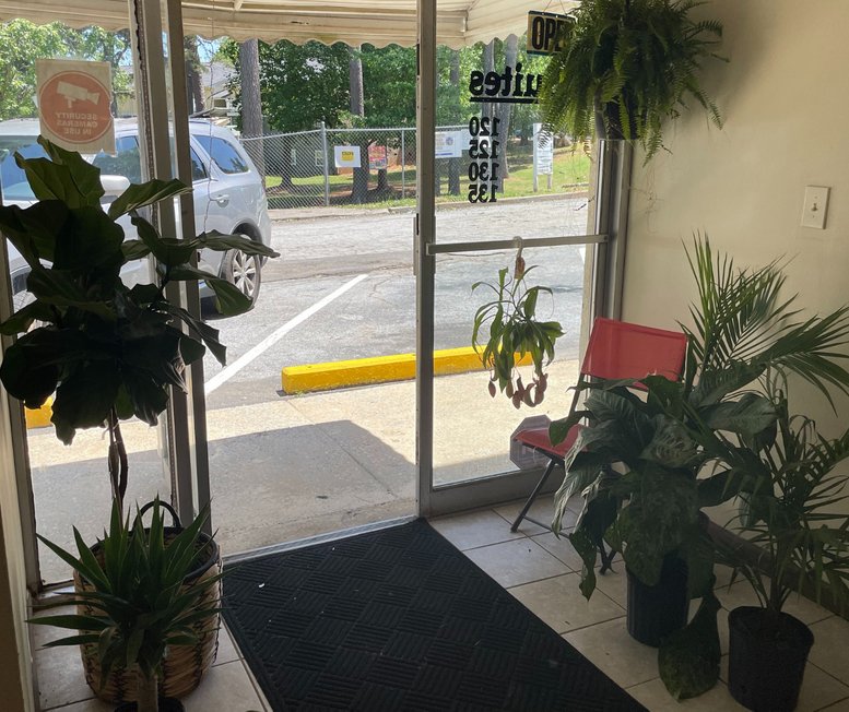 Main entrance of 5436 Riverdale Road 120, showing glass doors surrounded by vibrant greenery.