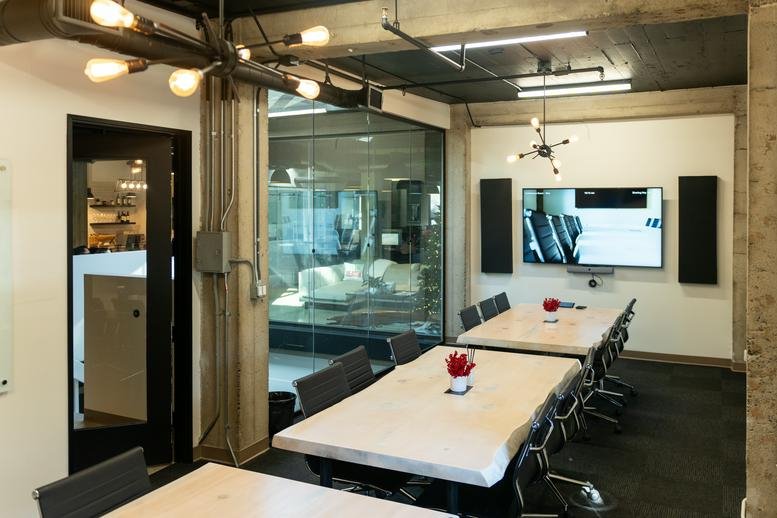 Meeting room at 580, Broadway Street, 201B with long white tables and a large wall-mounted monitor.