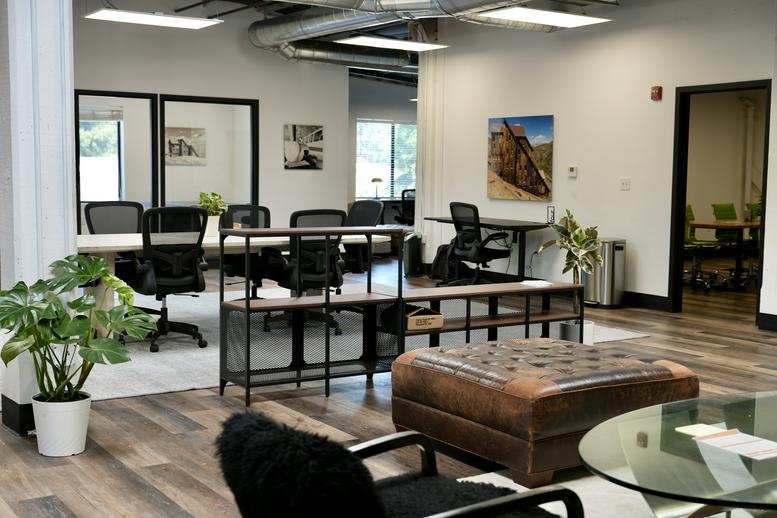 Spacious communal lounge and coworking area at 6780 Depot Street Suite 210 with leather ottoman and potted plants.