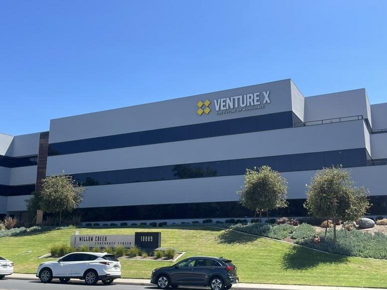 The exterior glass facade of the Venture X building at 10089 Willow Creek Road under a blue sky.