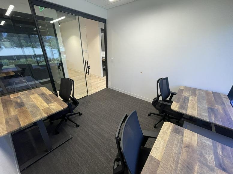 Bright two-person office with a long wooden desk and grey carpeting.