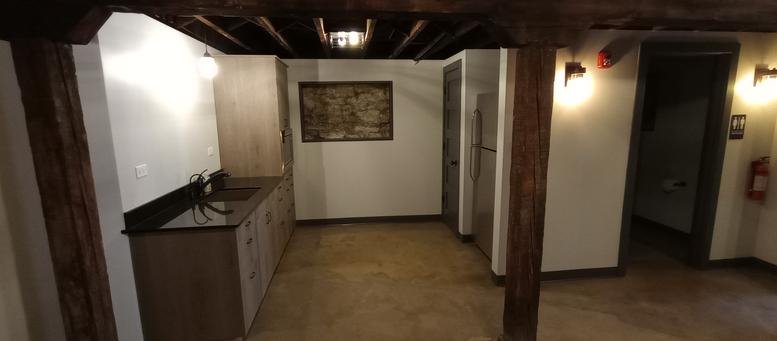 Communal kitchen area with dark countertops, wooden beams, and warm lighting.