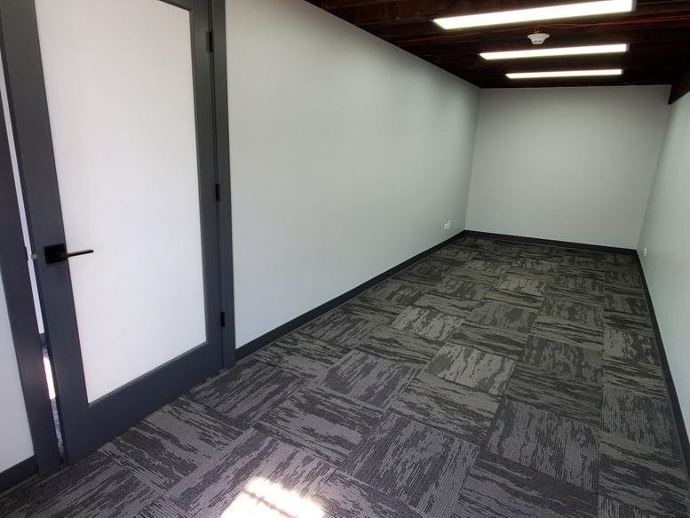 Bright private office featuring grey patterned carpet and modern recessed lighting.
