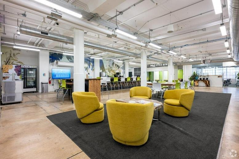 Spacious open-plan communal area with vibrant yellow armchairs and exposed ceiling pipes.