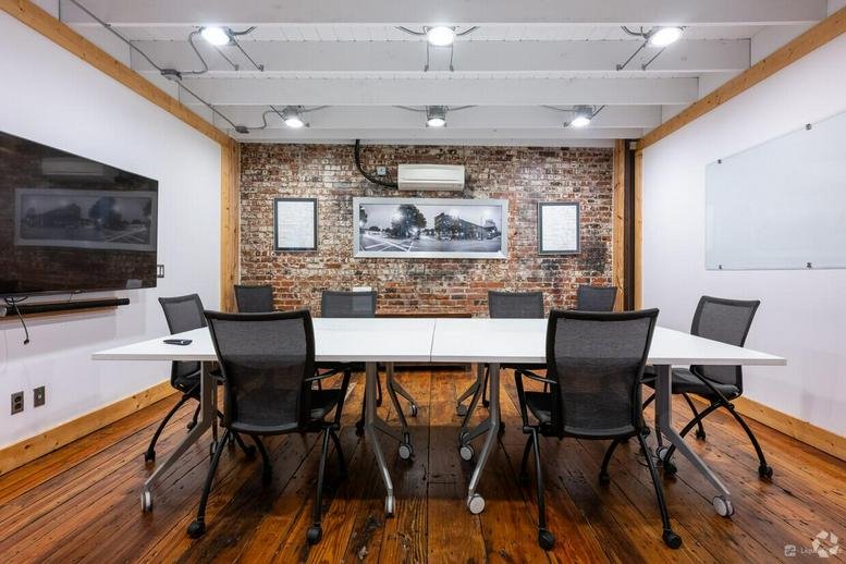 Spacious meeting room at 111 W Lewis St, Greensboro (Georgia) with white tables and an exposed brick wall.