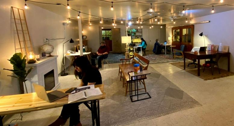 Spacious coworking area with warm string lighting, a white fireplace, and various workstations.