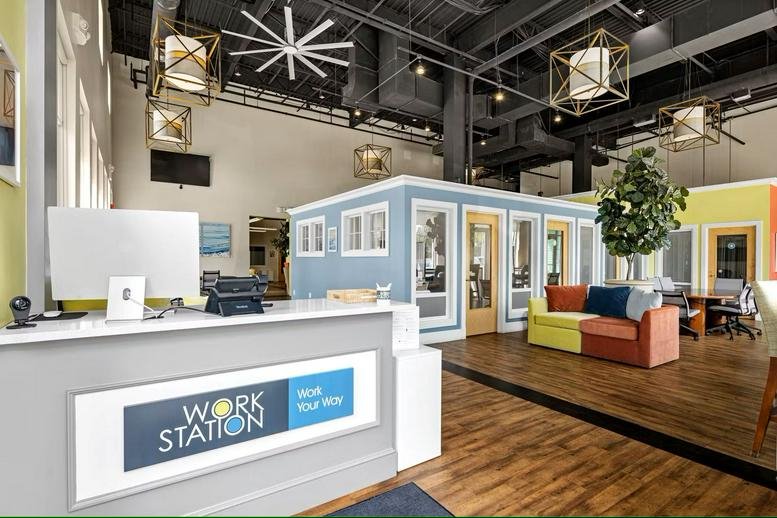 Spacious reception area with a branded front desk, colorful modular sofas, and high industrial ceilings.