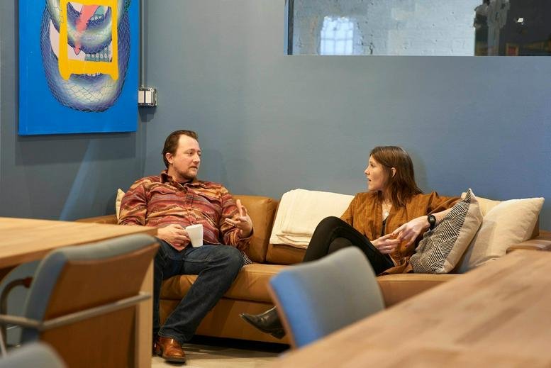 Coworking lounge at 1821 West Hubbard Street with people chatting on a tan sofa near blue feature walls.