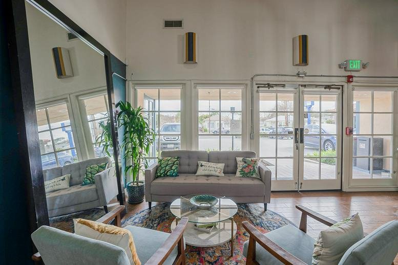Bright reception area with a grey sofa, glass coffee table, and large window-pane doors.