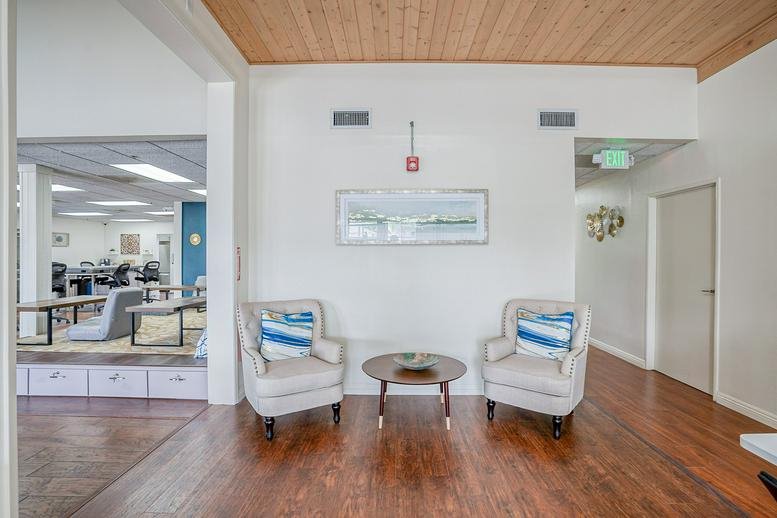 Waiting area with wood flooring and stylish white armchairs against a clean wall.