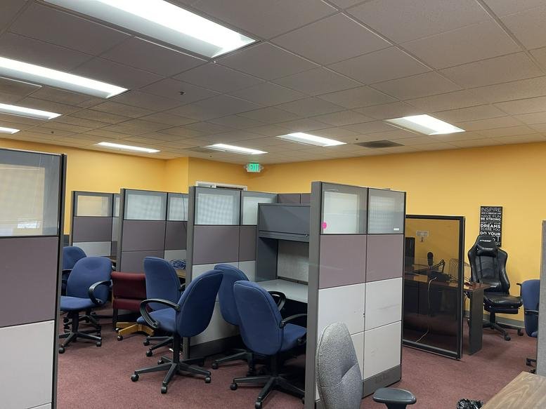 Spacious open office area featuring multiple cubicle workstations and blue rolling chairs.